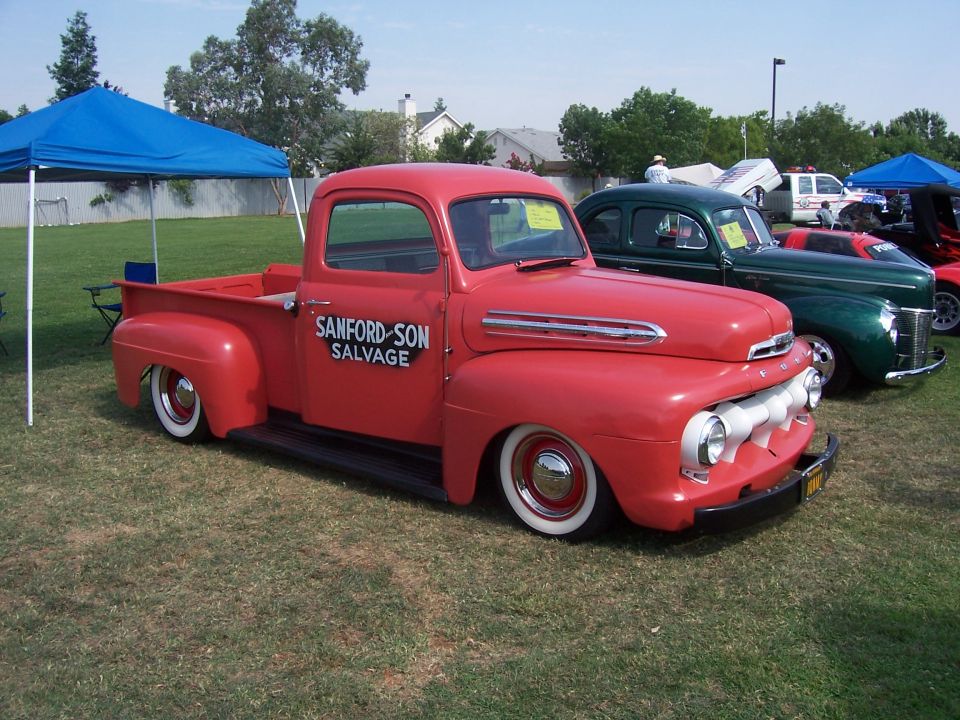 red pickup truck with 'SANFORD-SON SALVAGE' on door, parked next to green car