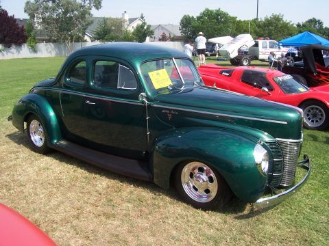 2002 Ford Mustang - A vintage green coupe is displayed at an outdoor event with other vehicles in the background.