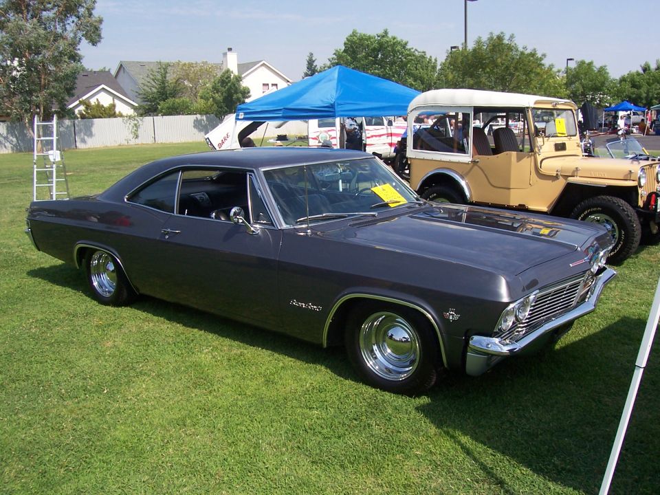 Dark gray 1965 Chevrolet Impala parked on grass next to a tan Jeep
