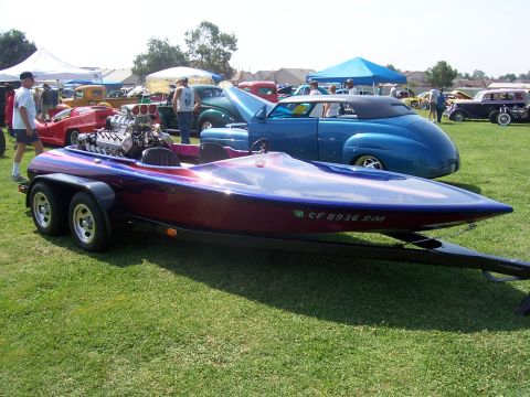 2002 Ford Mustang - A custom speed boat with a powerful engine is displayed at an outdoor event with other vehicles.