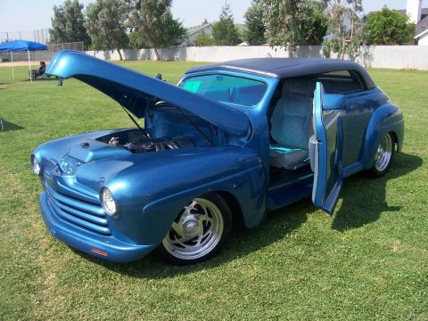2002 Ford Mustang - A custom blue hot rod sits on a grassy field with its hood and driver's door open, revealing the engine and interior.