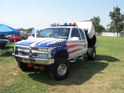 2002 Ford Mustang - A modified pickup truck with patriotic paint and emergency lights sits on a grassy field.
