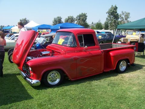 2002 Ford Mustang - Customized 1955 Chevrolet pickup truck displayed at an outdoor car show with other vehicles visible.