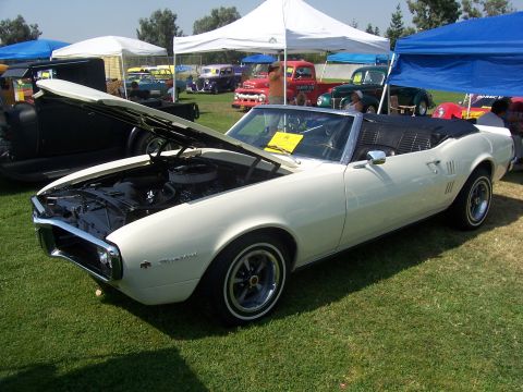 2002 Ford Mustang - A white 1967 Pontiac Firebird convertible is displayed with its hood open at an outdoor car show, with other vehicles and tents in the back…