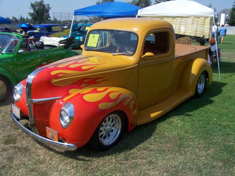 2002 Ford Mustang - A custom pickup truck with a bright flame paint job is displayed at an outdoor event.