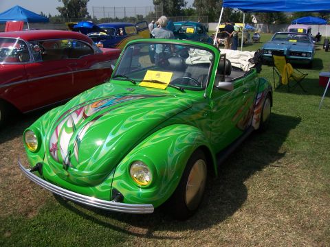 2002 Ford Mustang - A custom green Volkswagen Beetle with flame graphics is displayed at an outdoor car show.