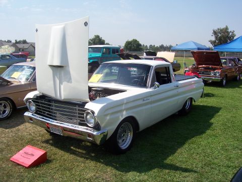2002 Ford Mustang - A classic white pickup truck is displayed with its hood open at an outdoor event, surrounded by other vehicles.