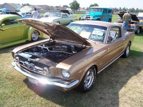 2002 Ford Mustang - A classic brown 1965 Ford Mustang coupe is displayed with its hood open, revealing the engine bay. Several other vehicles are parked nearby…