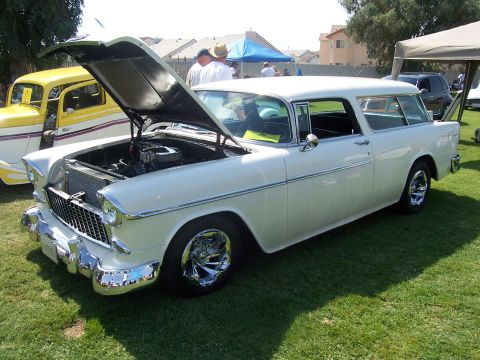 2002 Ford Mustang - A classic white station wagon from 1955 is displayed with its hood open, revealing the engine. Another yellow vehicle is visible to the lef…
