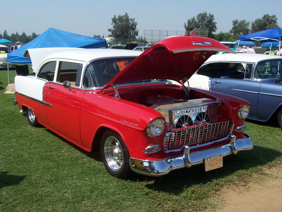 Red and white 1955 Chevrolet sedan, hood open, showing engine and chrome grille