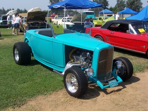 2002 Ford Mustang - A turquoise hot rod with a prominent grille and exposed engine sits on display at an outdoor car show.