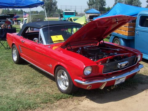 2002 Ford Mustang - A bright red 1965 Ford Mustang convertible is displayed with its hood open, revealing the engine bay.