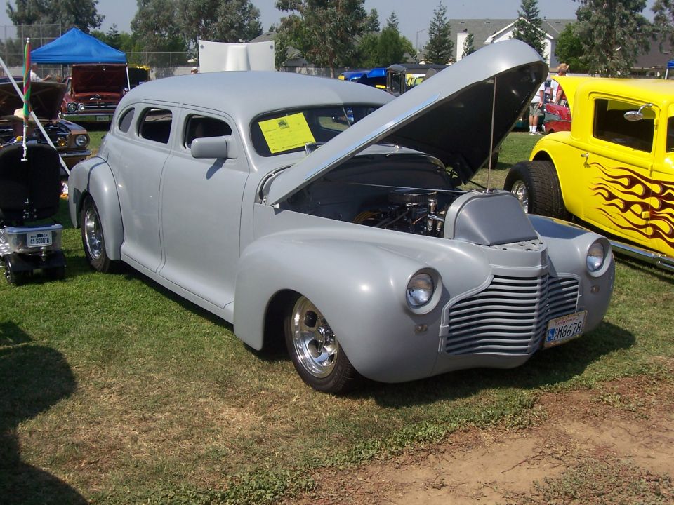Gray sedan with hood open, showing engine. Yellow hot rod with flames parked nearby