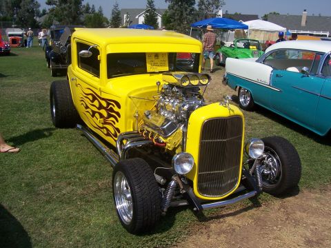 2002 Ford Mustang - A bright yellow hot rod with a prominent engine and flame graphics is parked on grass next to other vehicles.