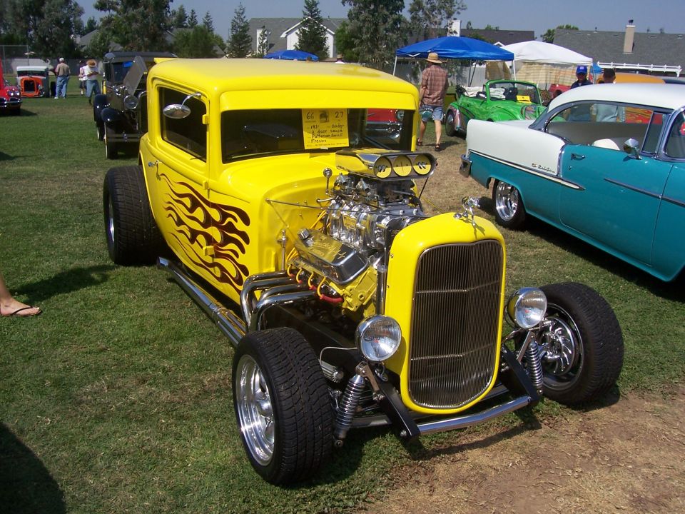 Yellow hot rod with flame decals on the side, exposed engine, and chrome grille