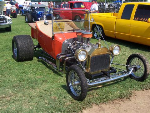 2002 Ford Mustang - A vintage hot rod with a prominent gold grille and exposed engine sits on display on a grassy field.