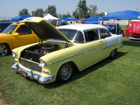 2002 Ford Mustang - A classic two-tone sedan is displayed with its hood up, revealing the engine bay, at an outdoor car show.