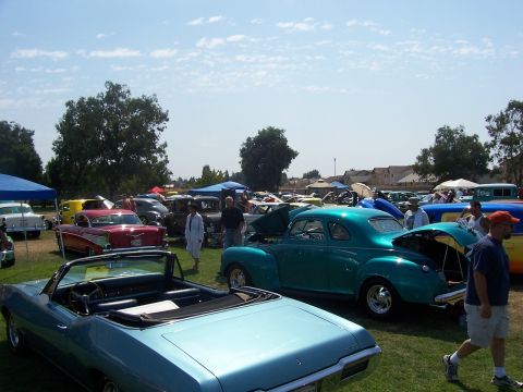 2002 Ford Mustang - Multiple classic cars are displayed on a grassy field under a partly cloudy sky.