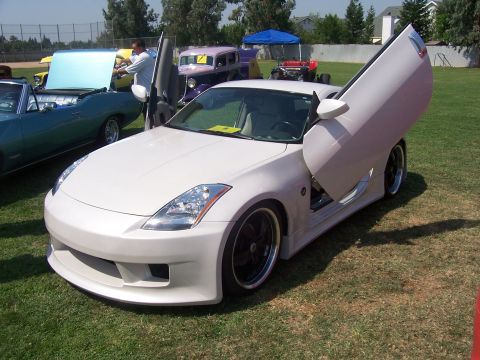2002 Ford Mustang - White sports car with butterfly doors on display at an outdoor car show.