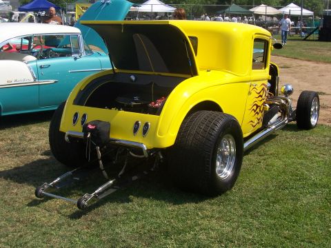2002 Ford Mustang - A yellow hot rod coupe is parked on grass next to a teal and white classic car.
