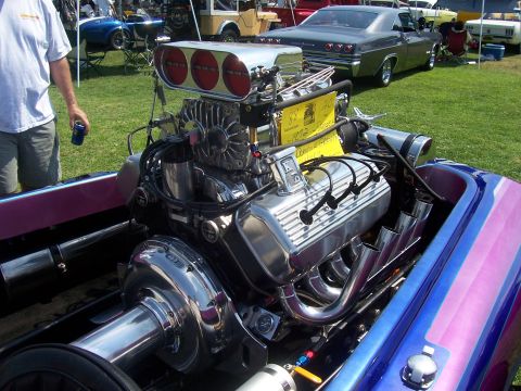 2002 Ford Mustang - A powerful V8 engine with a prominent supercharger and exhaust headers is installed in a boat, with other vehicles visible in the backgroun…