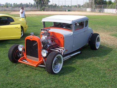 2002 Ford Mustang - A yellow Ford Mustang is parked next to a custom hot rod on a grassy field.