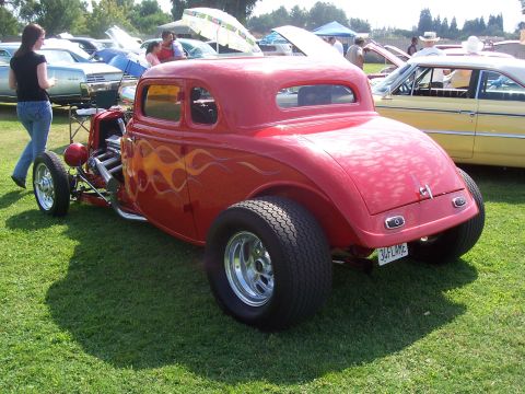 2002 Ford Mustang - A red hot rod with flame decals is parked on the grass at a car show.