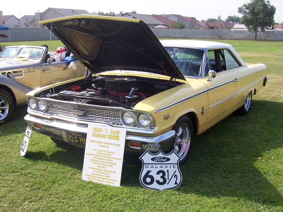 Yellow 1963 Ford Galaxie 500 XL with hood open, parked on grass next to another car