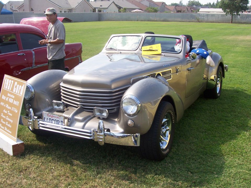1937 Cord convertible with a sign detailing its specs. Another car is partially visible to the left