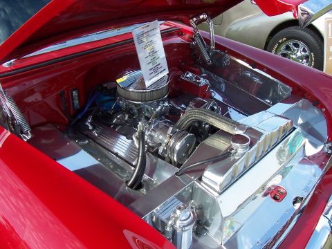 2002 Ford Mustang - The engine bay of a red car features extensive chrome detailing and a display document, with another vehicle visible in the background.