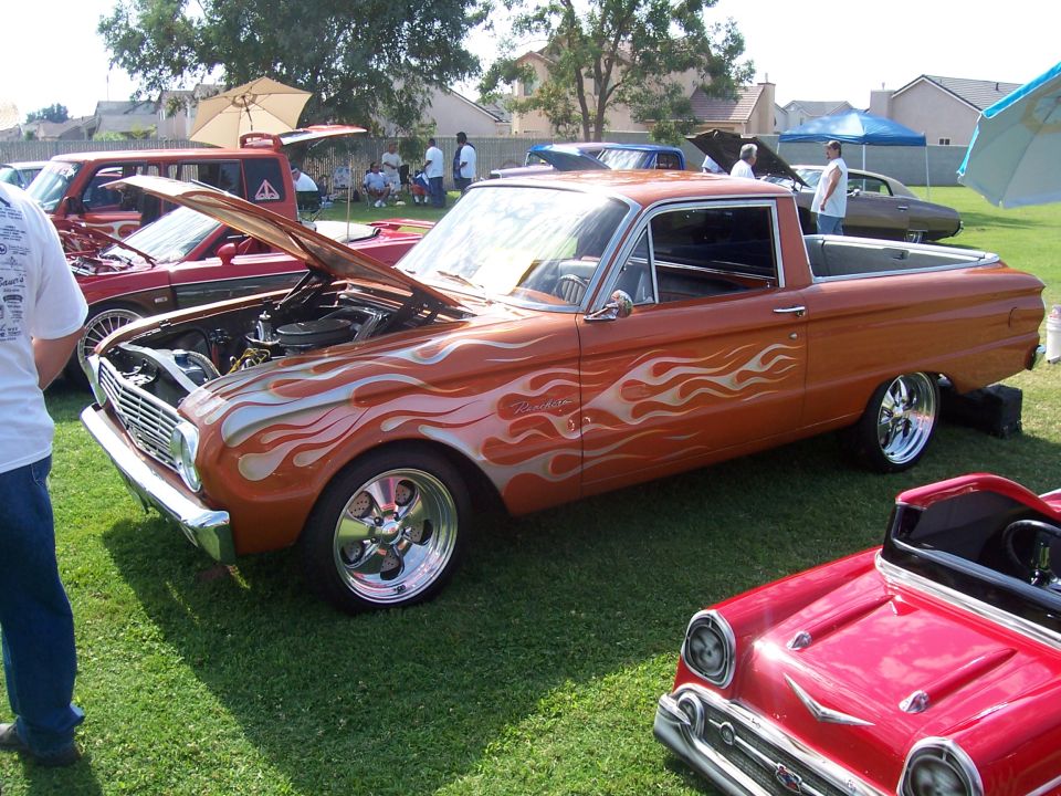 Orange pickup truck with silver flame decals, hood open, parked on grass next to a red car