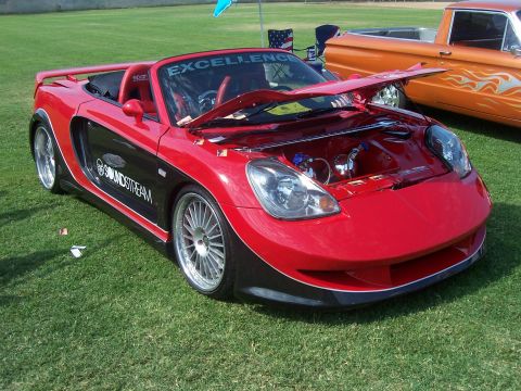 2002 Ford Mustang - A red and black convertible sports car is displayed with its hood open, alongside an orange pickup truck.