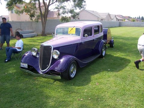 2002 Ford Mustang - A vintage sedan hot rod is displayed on a grassy lawn, hitched to a small trailer.