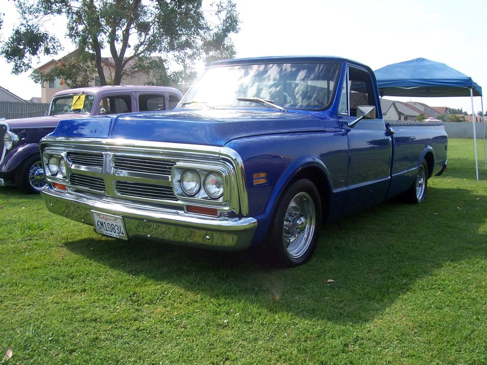 Blue 1970s pickup truck front 3/4 view. Another car is visible behind it