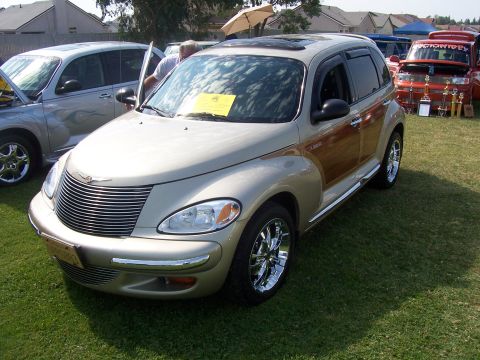 2002 Ford Mustang - A gold Chrysler PT Cruiser with wood paneling and chrome wheels is displayed on a grassy field, with other vehicles in the background.