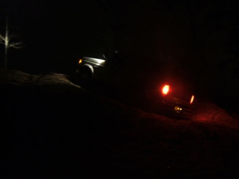 1989 Ford Bronco - A vehicle navigates a dark, unpaved road with its lights illuminating the path ahead.