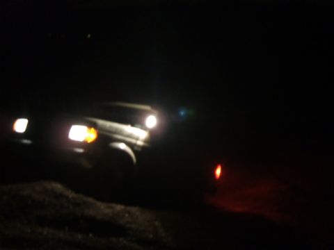 1989 Ford Bronco - A vehicle's headlights illuminate the darkness as it drives off-road at night.