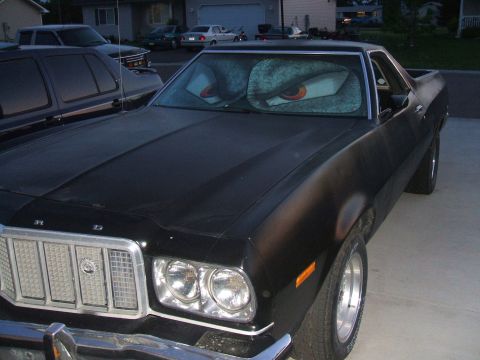 1974 Ford Ranchero - This black 1974 Ford Ranchero features a unique sunshade with cartoon eyes, adding a playful touch to the vehicle's front view.