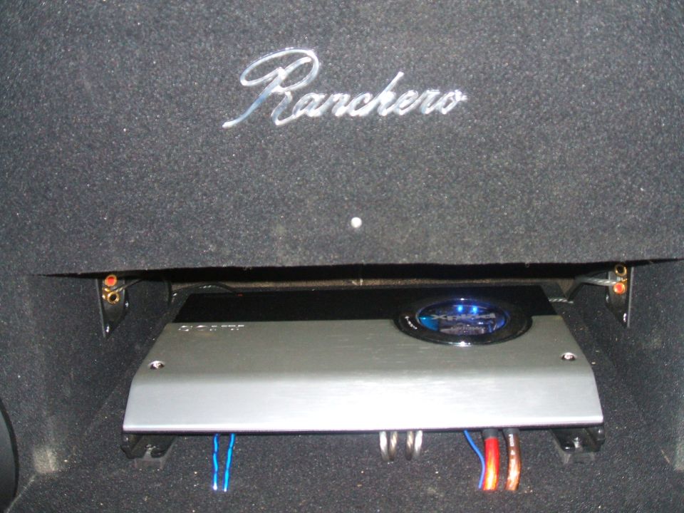 Car interior trim with chrome text 'Ranchero' above a silver car audio amplifier with blue illuminated logo