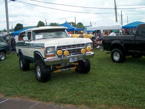 1978 Ford Bronco - A lifted 1978 Ford Bronco is parked on the grass at an outdoor event with other vehicles and tents in the background.