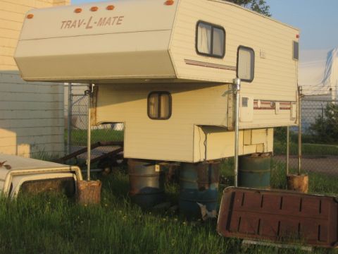 1996 Dodge 2500 - A slide-in truck camper is parked in a grassy area, supported by barrels and wooden blocks.