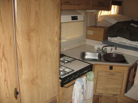 1996 Dodge 2500 - The interior of a camper shows a compact kitchen area with a two-burner stove, double sink, and wooden cabinetry.