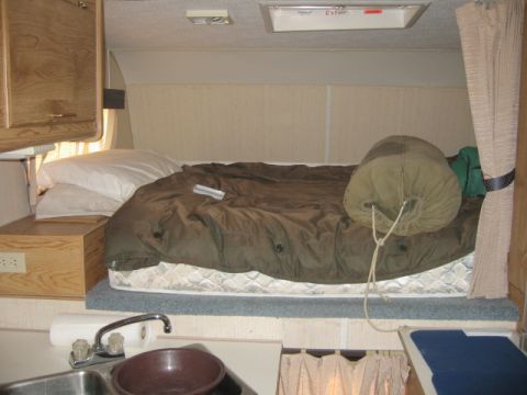 1996 Dodge 2500 - Interior view of a camper bed with a sleeping bag and pillows, next to a small sink area.