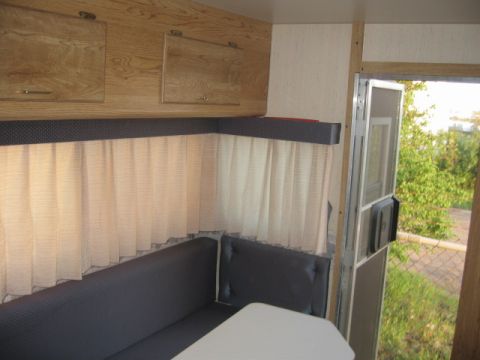 1996 Dodge 2500 - Interior view of a camper showing seating, curtains, and cabinets, with an open door revealing an outdoor scene.