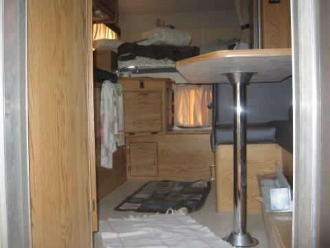 1996 Dodge 2500 - Interior view of a camper showing wood paneling, a table with a chrome pedestal, and a sleeping area with blankets.