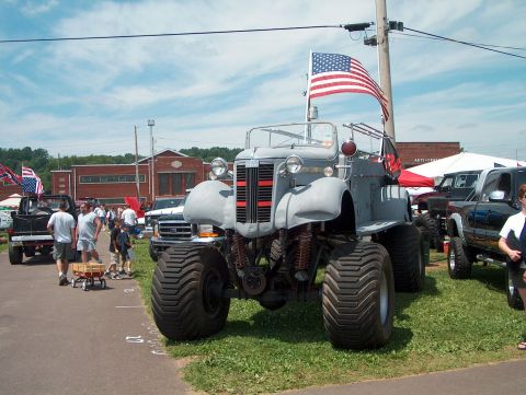 1978 Ford Bronco - A custom monster truck with oversized tires and an American flag is displayed at an outdoor event.