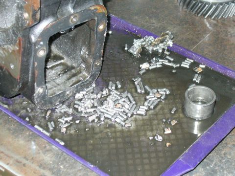 1978 Ford Bronco - A differential housing sits next to a pile of broken roller bearings and metal fragments in a mechanic's tray.