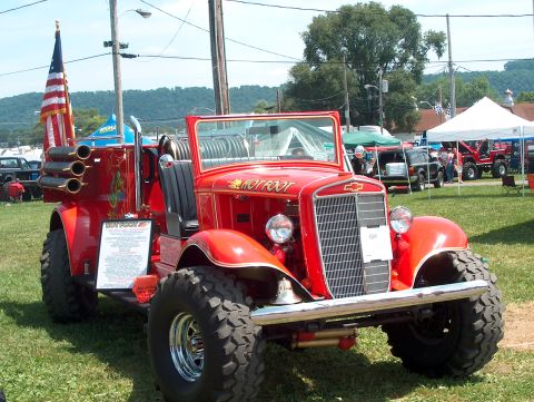 1978 Ford Bronco - A custom red truck, dubbed "HOT FOOT," displays its large tires and unique rear exhaust system at an outdoor event.