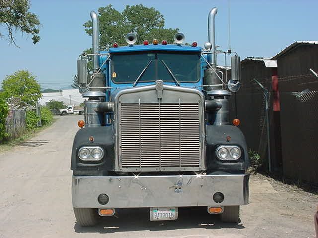 Front view of blue Kenworth semi truck with chrome grille and dual stacks on dirt lot