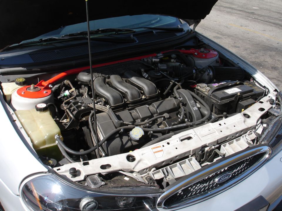 Car's engine bay with V6 engine visible. Red strut bar installed
